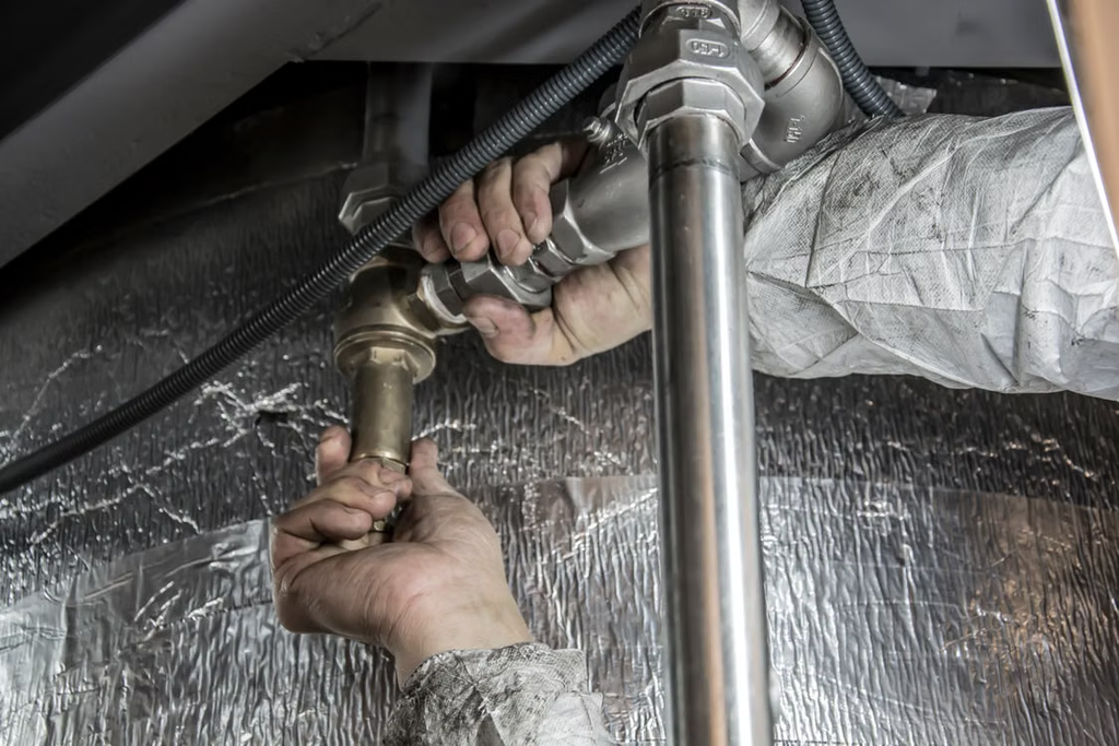 Close-up of a plumber's hands installing steel pipes indoors, showcasing skilled manual work. 